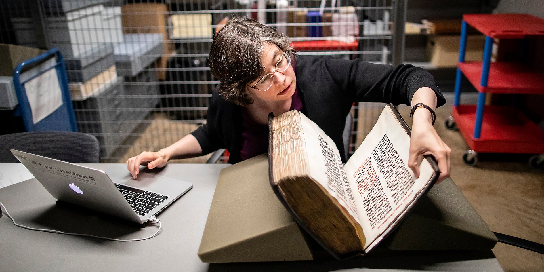 Woman with laptop examining large book