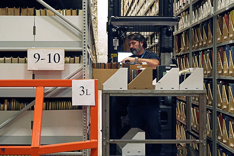 A library staff member retrieves a book from a cardboard tray among the shelves in LIBRA
